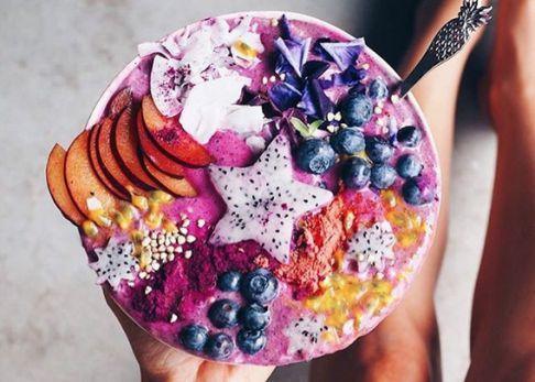 Tazón de smoothie rosa con trozos de fruta, arándanos, pitaya, y cuchara decorativa