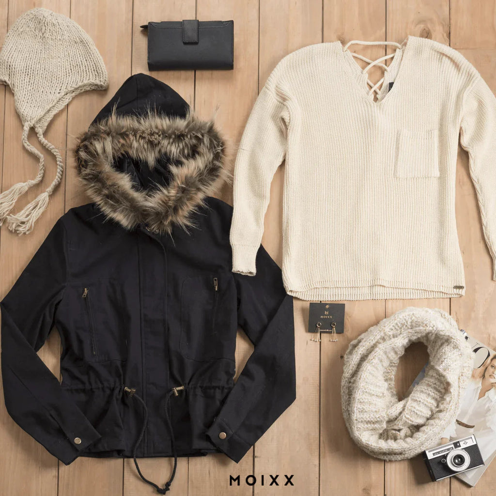 Conjunto de ropa de invierno con chaqueta negra con capucha de piel, suéter beige, gorro, bufanda tejida y accesorios sobre fondo de madera