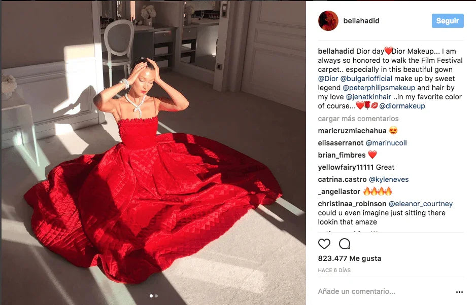Mujer sentada en el suelo con vestido largo rojo brillante en habitación iluminada con sillas y muebles blancos