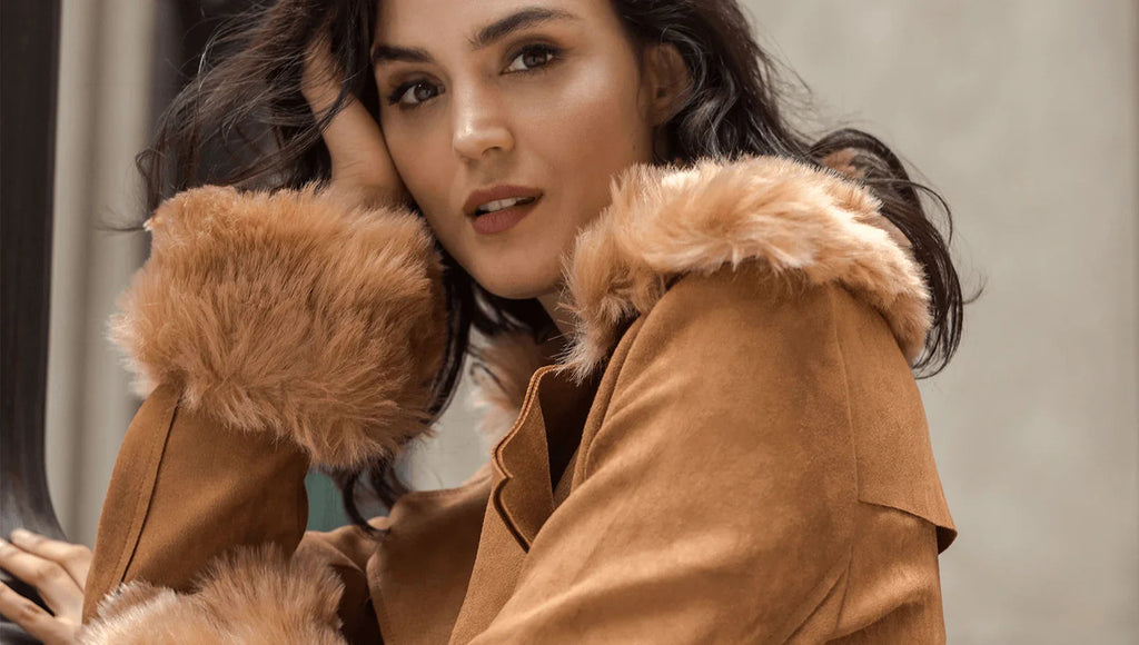 Mujer con abrigo marrón de gamuza con cuello y puños de peluche, posando con fondo neutro