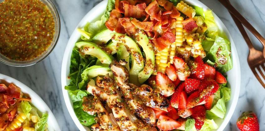 Ensalada fresca con lechuga, pollo a la parrilla, tocino, maíz, fresas y aderezo en bol blanco sobre mesa de mármol