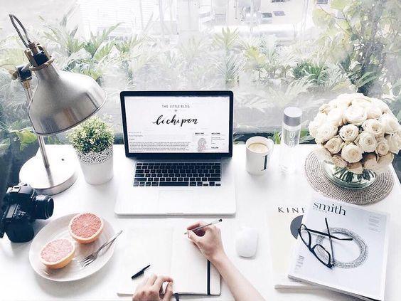 Escritorio luminoso con laptop, flores blancas, cuaderno, cámaras y pomelo partido para desayuno