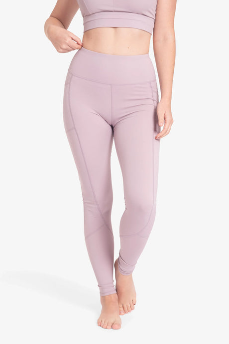 Mujer con leggings deportivos color lila de talle alto en fondo blanco, sin calzado