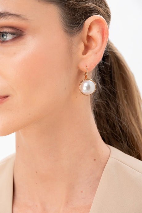 Pendiente dorado con perla grande en oreja de mujer con piel clara y cabello recogido